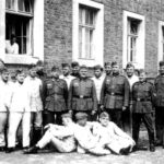 Группа инструкторов в полевой форме одежды сфотографировалась на фоне казармы на память с молодыми бойцами