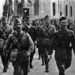 Албанские партизаны маршируют по улицам освобожденной Тираны, ноябрь 1944 года. Обратите внимание на лейтенанта (слева на переднем плане), знаки различия которого расположены на предплечье.